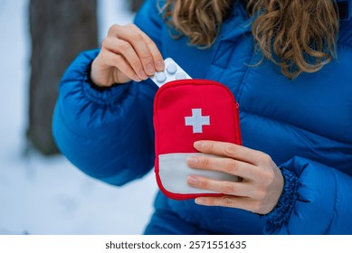 Primer plano de las manos de una mujer tomando píldoras de un botiquín de primeros auxilios rojo con una cruz blanca. Mientras está de pie en un bosque de invierno nevado. Subrayando la importancia de la preparación para las actividades al aire libre