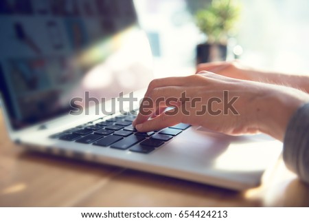 Closeup woman's hands typing on a laptop on a wooden desk with sunlight.