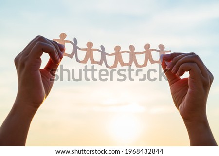 Closeup woman's hands unfold the paper human chain over the sunset sky to see the result after finish cutting, teamwork concept