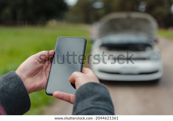 Close-up of a woman\'s hands using a cell phone\
to call for help with her broken\
car