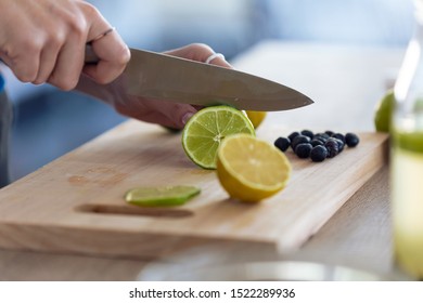 Close-up of woman's hands while she cutting limes over wooden table in the kitchen.