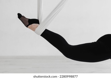 Close-up of a woman's legs in black tights performing an Inverted anti-gravity Aerial yoga with the use of aerial silks or fabrics, Balance between physical and mental effort. Isolated on white. - Shutterstock ID 2280998877