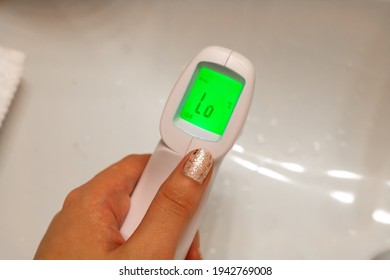 Closeup Of A Woman's Manicured Hand Holding A Digital Forehead Temperature Scanner - Thermometer - With A Low Human Body Temperature. Quarantine Instrument.