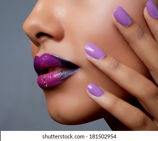 Close-up of woman's mouth with dark fashion purple lipstick with ombre effect. Hand with purple nailpolish touching tanned face 