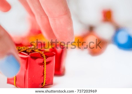 Close-up of women hand take a red xmas gift with blurred colorful balls and Christmas decor in background. Christmas and New Year concept with copy space. Christmas greeting card.