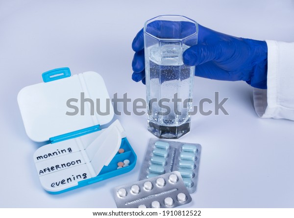 Closeup of women hand taking pills.  Pill\
boxes with tablets and glass of water on white background.\
Medication in medical clinic. Drugs use for\
treatment.