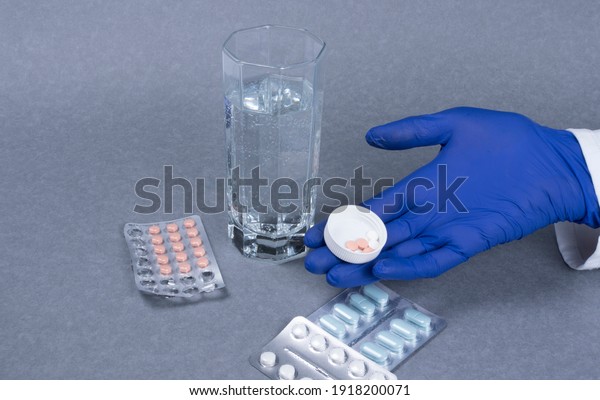 Closeup of women hand taking pills.  Pill
boxes with tablets and glass of water on gray background.
Medication in medical clinic. Drugs use for
treatment.