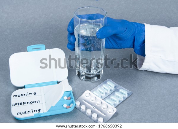 Closeup of women hand taking pills. 
Pill boxes daily with pills and glass of water on grey background.
Medication in medical clinic. Drugs use for
treatment.