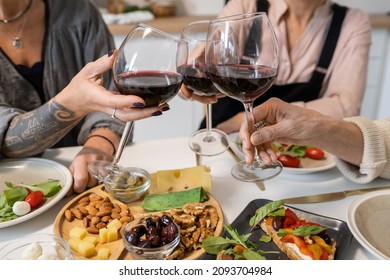 Close-up of women toasting with glasses of red wine while sitting at dining table with appetizers - Powered by Shutterstock