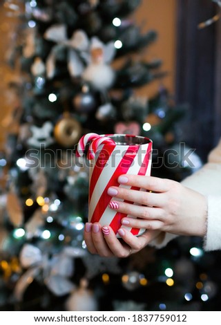 Close-up of women's hands holding a Christmas box and lollipops. Sweets in the hands of a woman on the background of a twinkling Christmas tree. Small depth of field with emphasis on hands and nails.