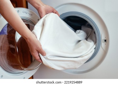 Close-up of women's hands pulling clean white linen clothes out of the washing machine after washing in the bathroom.Women's hands put the laundry in the washing machine.Routine homework.Laundry day. - Powered by Shutterstock