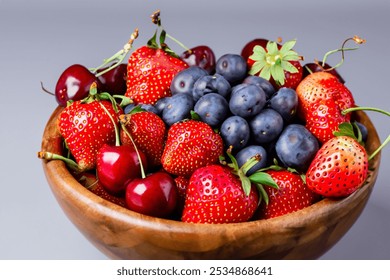 Close-up of a wooden bowl filled with strawberries, blueberries, and cherries on a grey background - Powered by Shutterstock