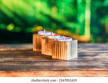 Close-up Of Wooden Candle Holders With Tea Light On Red Rose Petals And Blurred Green Background.