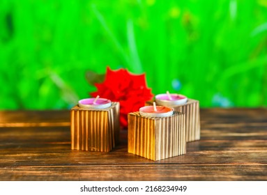 Close-up Of Wooden Candle Holders With Tea Light On Red Rose Petals And Blurred Green Background.