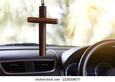 Closeup wooden crucifix hang  in  front steering wheel and console of the car. Concept, talisman,amulet to prevent accidents. Belief, faith,holy  in god to protect when driving.                       