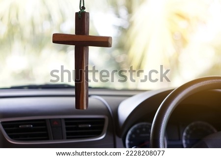 Closeup wooden crucifix hang  in  front steering wheel and console of the car. Concept, talisman,amulet to prevent accidents. Belief, faith,holy  in god to protect when driving.                       