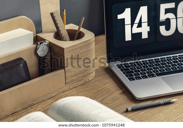Close-up of wooden desk organizer\
with pencil and watch, computer, pen and book lying on the\
desk