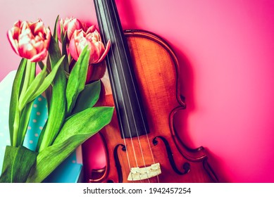 Close-up of wooden handmade musical instrument with fresh bouquet of flowers on pink background. Joy of art and nature. Romance, music and artistry concept, copy space