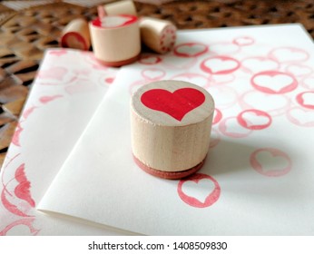 Closeup of a wooden heart stamp for making handmade cards. More stamps in the background and cards stamped with hearts in red ink.