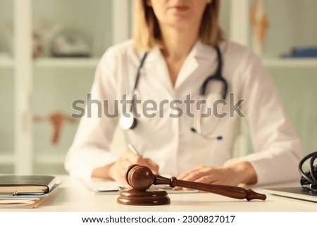 Close-up of wooden judge gavel on table female doctor doing paperwork on background. Litigation, malpractice and forensic concept