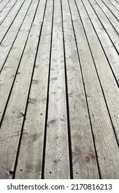 Closeup Of A Wooden Plank Surface. Light Grey Vintage Flooring With Slats Forming An Outdoor Terrace. Old Textures Of Hard Wood Floor Used As A Walkway Or Deck. Long Vertical Outdoor Floorboards