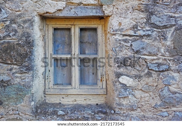 Closeup of a wooden window in a stone wall of
an old grey house. Boarded up square window frame in a historic
rustic building. Architecture and background of a rural structure
outside with copyspace