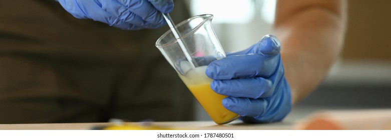 Close-up Of Woodworker Hands Making Wood Varnish At Workshop. Specialist In Gloves Mixing Liquor With Dropper In Transparent Beaker. Carpentry Work Concept