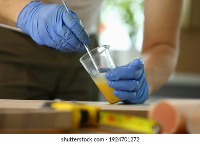 Close-up Of Woodworker Hands Making Wood Varnish At Workshop. Specialist In Gloves Mixing Liquor With Dropper In Transparent Beaker. Carpentry Work Concept