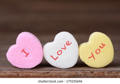 Closeup of the words I Love You spelled out on candy hearts. Three hearts on a rustic wood background. Great for Valentine's Day projects.