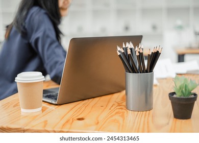 Close-up of a work desk with a laptop, a cup of coffee, pencils, and a small potted plant, exemplifying a contemporary workspace. - Powered by Shutterstock