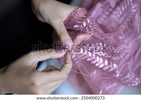 Close-up of work process of a tailor in her boutique. Clothes shop for wedding dresses and kebaya. Designer hands sewing kebaya. Hands of woman sew beads and white lace on mannequin or bride.


