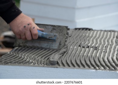 Close-up Of Worker Hand, With Trowel Applying Glue On White Rigid Polyurethane Foam Sheet For House Insulation. 