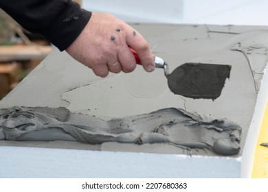 Close-up Of Worker Hand, With Trowel Applying Glue On White Rigid Polyurethane Foam Sheet For House Insulation. 