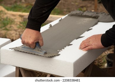 Close-up Of Worker Hand,  With Trowel Applying Glue On White Rigid Polyurethane Foam Sheet For House Insulation.