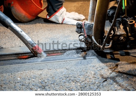 Close-up of a worker heating a tram rail with a torch during welding repair on a city street at night, illustrating night-time railway track maintenance and rail welding.