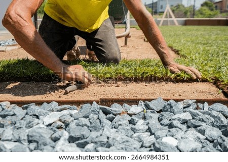 Close-up of worker manually installing turf with knife near a gravel path. Perfect for themes on landscaping, outdoor renovation, and manual craftsmanship