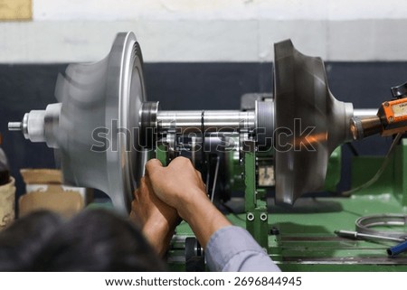 Close-up of a worker operating a dynamic balancing machine, adjusting the high-speed rotating turbine or fan component in a heavy industrial factory environment.