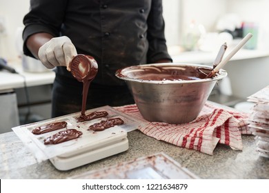 Closeup of a worker pouring melted chocolate into molds while standing at a table in an artisanal chocolate making factory - Powered by Shutterstock