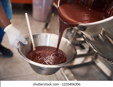 Closeup of a worker pouring melted chocolate from a mixer into a container while working in an artisanal chocolate making factory  - Powered by Shutterstock