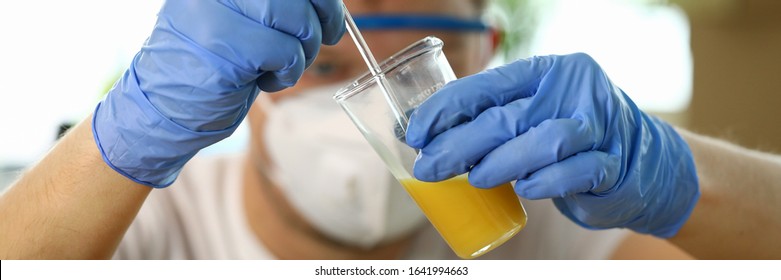 Close-up Of Worker In Respirator Dripping Liquor Drops To Beaker With Wood Varnish. Specialist In Eyeglasses And Gloves Working In Lab. Exact Proportions And Mixing Ratio Concept