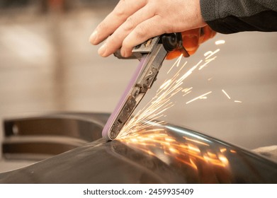 Close-up of worker using angle grinder on metal without protecting gloves, creating sparks in workshop
