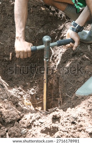 Close-up of a worker using a manual soil auger to drill the ground. Concept of soil testing, agriculture work, geotechnical survey, construction preparation, and manual labor outdoors.