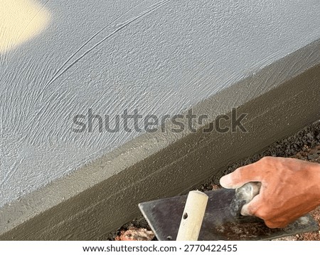A close-up of a worker using a metal hand trowel to create a smooth, finished edge on a freshly poured concrete curb or wall.