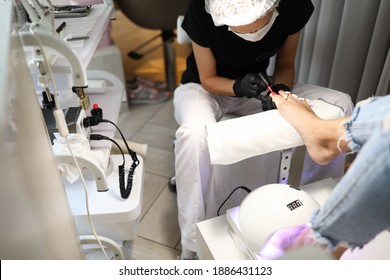 Close-up of worker using professional tools. Chiropodist using protective gloves and mask. Woman covering toe nails with bright nail polish. Beauty salon and chiropody concept