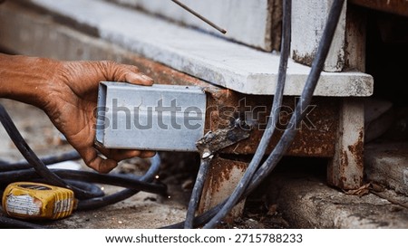 Close-up of a worker's bare hand holding a metal tube during unsafe welding on a rusty structure. Concept of industrial safety hazards, lack of protective gear, and high risk of electrical burns.