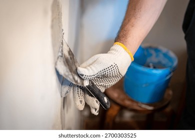 Close-up of a worker's gloved hand using a small putty knife to press thick patching compound firmly into a hole in the interior wall.