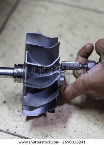 Close-up of a worker's hand using a bor tuner or borcun to perform a correction or balance adjustment on the metal blades of a turbocharger compressor wheel.