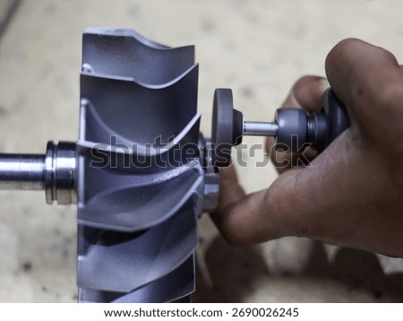 Close-up of a worker's hand using a bor tuner or borcun to perform a correction or balance adjustment on the metal blades of a turbocharger compressor wheel.
