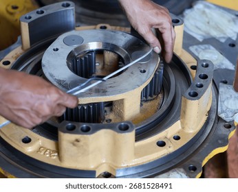 Close-up of a worker's hands assembling a seal piston, focusing on the intricate metal gears and parts in a workshop environment.