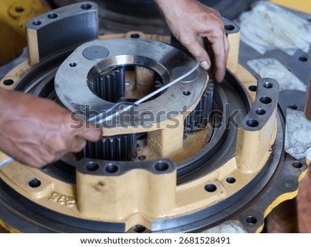 Close-up of a worker's hands assembling a seal piston, focusing on the intricate metal gears and parts in a workshop environment.